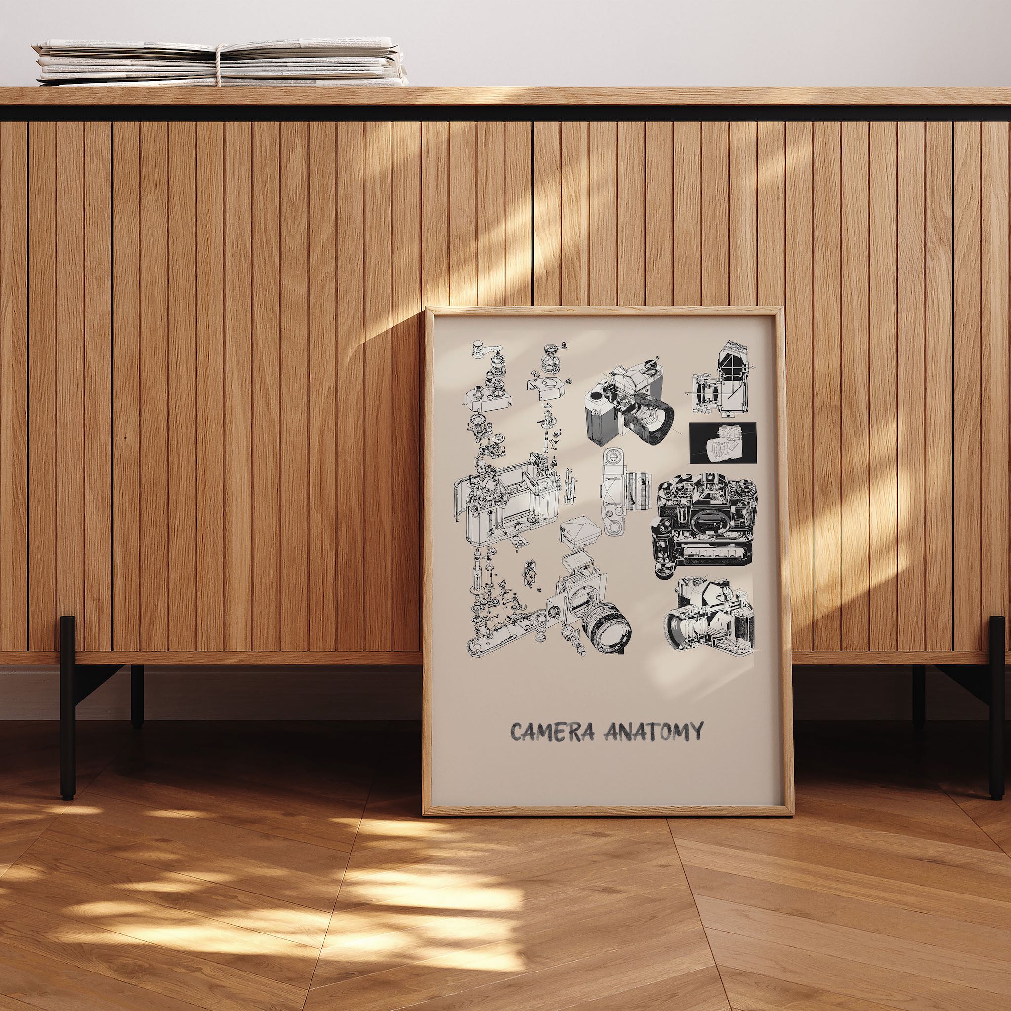 Camera Anatomy’ başlıklı siyah-beyaz kamera teknik çizimi posteri, modern bir iç mekanda yere yaslanmış çerçeveli olarak sergilenmiş.